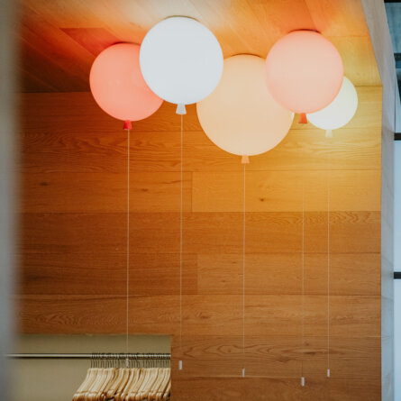 A modern ceiling light installation featuring round, balloon-like lights in red and white hues, hanging from the wooden ceiling of a contemporary room.