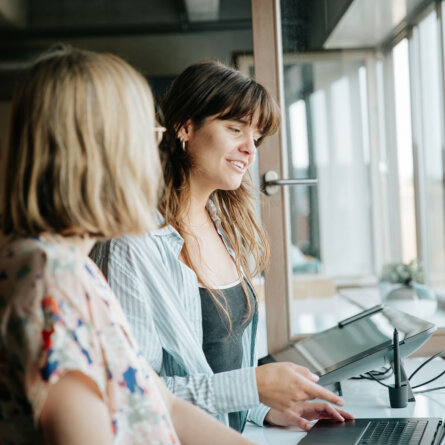 Two women collaborating on a laptop discussing AI strategies.