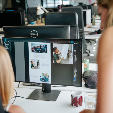 A computer screen displaying project implementation designs with two people discussing in the background.