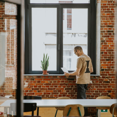 A Hyperion team member working on a laptop by a large window in a brick-walled room, emphasizing a blend of modern technology in a historical setting.